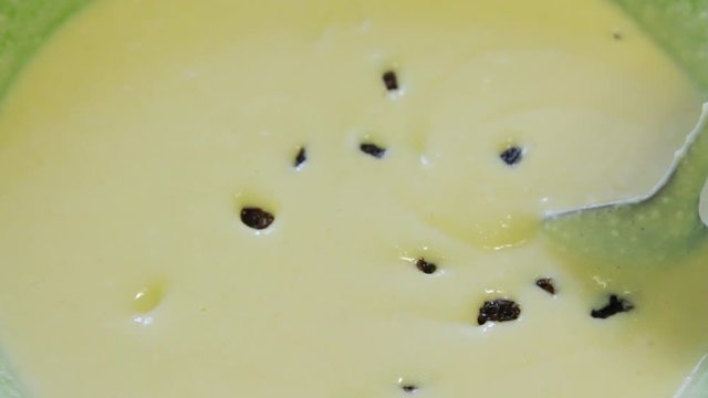 Extreme close-up of dough into which brown raisins fall, the cook mixes a tablespoon of dough and raisins.