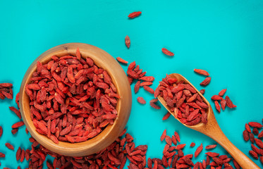 Goji berries in wooden bowl on aqua background, top view