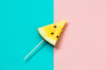 cut off triangular slice of ripe yellow watermelon on pink-blue background