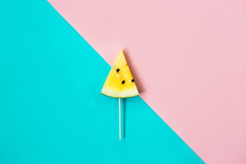 cut off triangular slice of ripe yellow watermelon on pink-blue background
