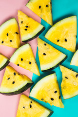 cut off triangular slices of ripe yellow watermelon on pink-blue background