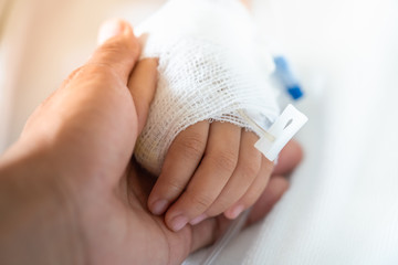 Closeup parent holding child's hand with saline solution to give encouragement.