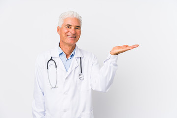Mature caucasian doctor man showing a copy space on a palm and holding another hand on waist.