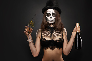 Fototapeta na wymiar Halloween girl with skull makeup for Halloween on a black background holds champagne in her hands