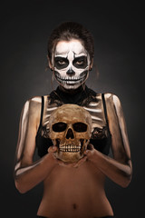 Halloween girl with skull makeup for Halloween on a black background holds a human skull in her hands