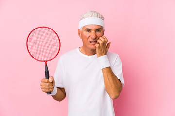 Naklejka premium Middle aged man playing badminton isolated biting fingernails, nervous and very anxious.