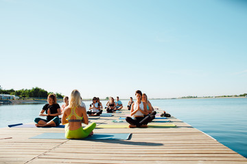 in the morning a group of people do yoga on the pier by the lake