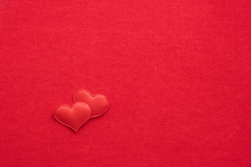 2 small textile red hearts are nearby on a background of red velvet paper.