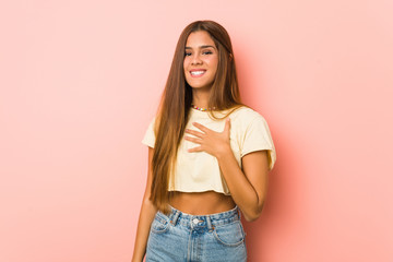 Young slim woman laughs out loudly keeping hand on chest.