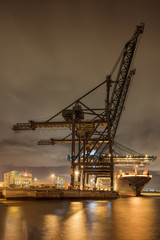 Fototapeta na wymiar Night scene with illuminated container terminal, massive crane and moored vessel, Port of Antwerp, Belgium.