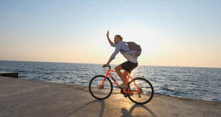 Fototapeta na wymiar Young handsome male in casual wear ride on the colorful bicycle on the morning beach against beautiful sunset and the sea
