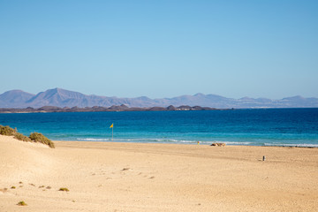 View on sand dune beach from Vuerteventura with Lanzarote and Lobos canary island in the background - golden  yellow sand dunes light blue sky summer season holiday travel vacation seascape mountains