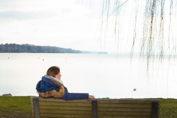 Lady sit on a bench at the lake shore admiring the beautiful landscape view.