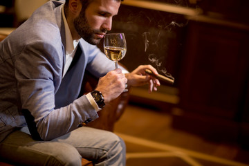Young man tasting white wine and smoking cigar