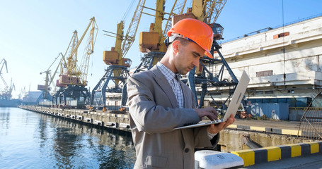 Young male worker of sea harbor in helmet, cargo manager in suit and halmet works outdoor , cranes...