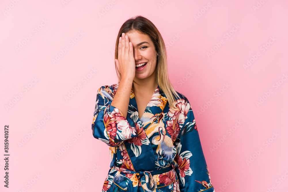 Wall mural young caucasian woman wearing pajamas having fun covering half of face with palm.