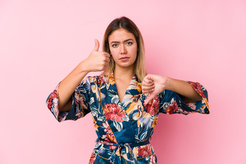 Young caucasian woman wearing pajamas showing thumbs up and thumbs down, difficult choose concept