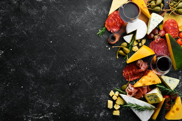 Fototapeta na wymiar Italian appetizers. Cheese, wine, salami and prosciutto on a black stone background. Top view. Free space for your text.