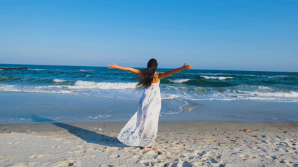 Fototapeta na wymiar Young beautiful woman dressed in a white dress walk barefoot on the summer beach 
