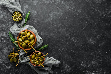 Capers. Marinated capers in a bowl on a black stone background. Top view. Free space for your text.