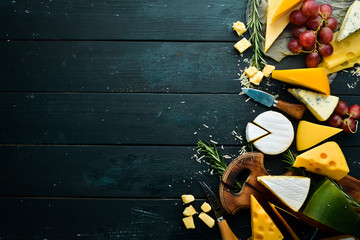 Variety of cheese and cheese slicing on black wooden background. Top view. Free space for your text.