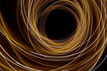 Long exposure light painting, vibrant gold color in abstract swirl against a clean black background.  Light painting photography.