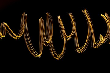 Long exposure light painting, vibrant gold color in abstract swirl against a clean black background.  Light painting photography.