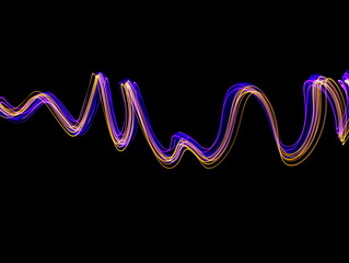 Long exposure light painting, vibrant purple and yellow color in abstract swirl against a clean black background.  Light painting photography.