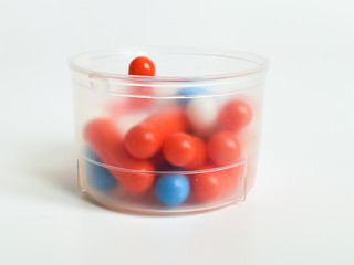 Capsules of different colors with medicine in a measuring Cup on a white background.