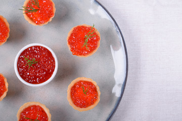 Red caviar served in shortbread tartlets and a ceramic bowl topped with dill on the round plate
