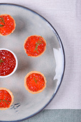 Red caviar served in shortbread tartlets and a ceramic bowl topped with dill on the round plate