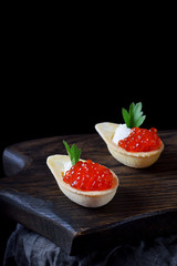Red caviar and ricotta cheese in the spoon shaped tartlets served on the wooden board