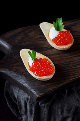 Red caviar and ricotta cheese in the spoon shaped tartlets served on the wooden board