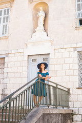 Young and beautiful brunette girl in dress and hat walking outdoor in the Old Town. Nice, France. Summer vacation, traveling and tourism.
