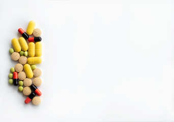 Multi-colored tablets and capsules of various shapes on the left along the edge with a place for text top view.