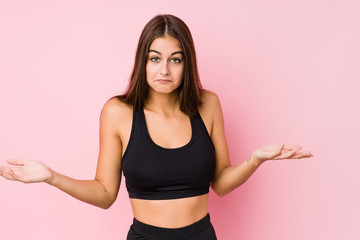 Fototapeta na wymiar Young caucasian fitness woman doing sport isolated doubting and shrugging shoulders in questioning gesture.