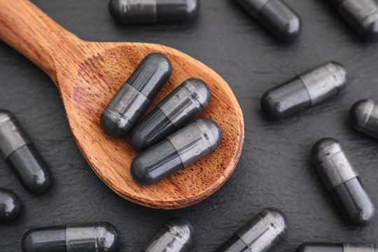 Activated Vegetable Charcoal Capsules In A Wooden Spoon