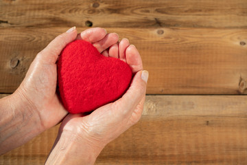Female hands giving a red heart on an old wooden table in vintage retro style