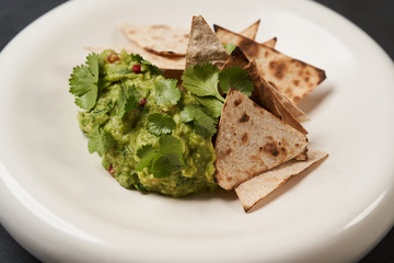 Guacamole with pita chips on white plate, close-up. Mexican guacamole