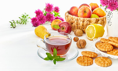Tea with herbs fruits and cookies. Still life with hot drink apple and nuts at white wooden board in rustic style.