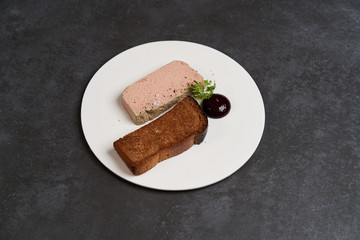 Toasted bread with pate in white plate on dark background with copy space, close-up.