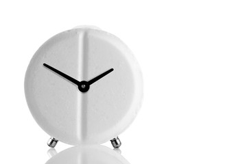 Round white pill in the form of an alarm clock on a mirror surface. Alarm clock - pill on white...