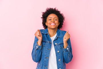 Young african american woman against a pink backgroound isolated raising fist, feeling happy and successful. Victory concept.