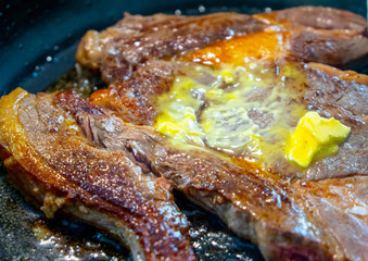 Cooking a big steak with butter on a black pan
