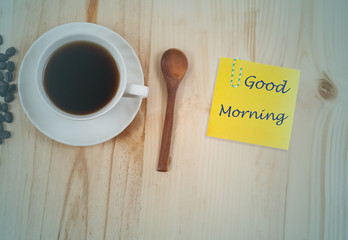 Good morning text with  white Cup of coffee on Pine wood desktop table on top view.