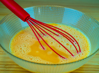 Batiendo huevos en un recipiente de cristal con una espumadera roja
