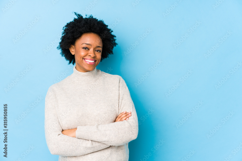 Wall mural middle aged african american woman against a blue background isolated smiling confident with crossed