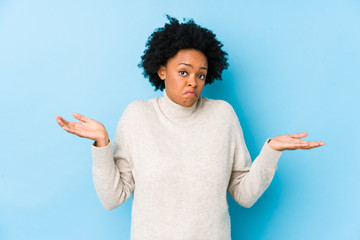 Middle aged african american woman against a blue background isolated doubting and shrugging...