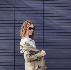 happy curly-haired woman in a jacket posing against a wall