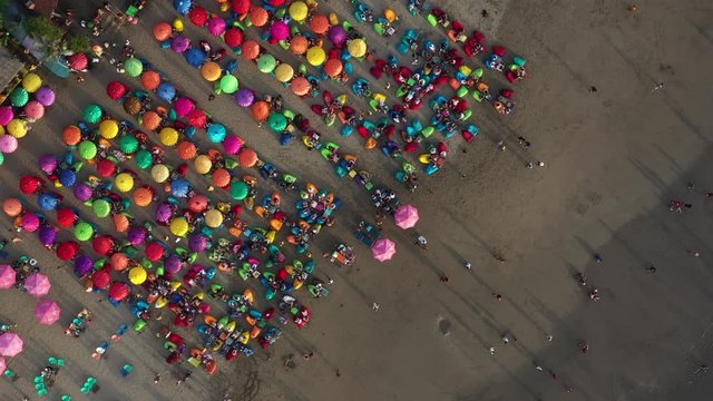 Colorful umbrellas on the sandy beach in Bali. Aerial corkscrew shot above the Double six beach with Parasols And Beanbags, Indonesia,